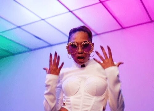 Person in stylish white outfit and funky sunglasses under colorful lighting.